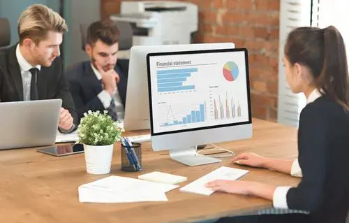 Equipe trabalhando em computadores com relatórios financeiros na tela